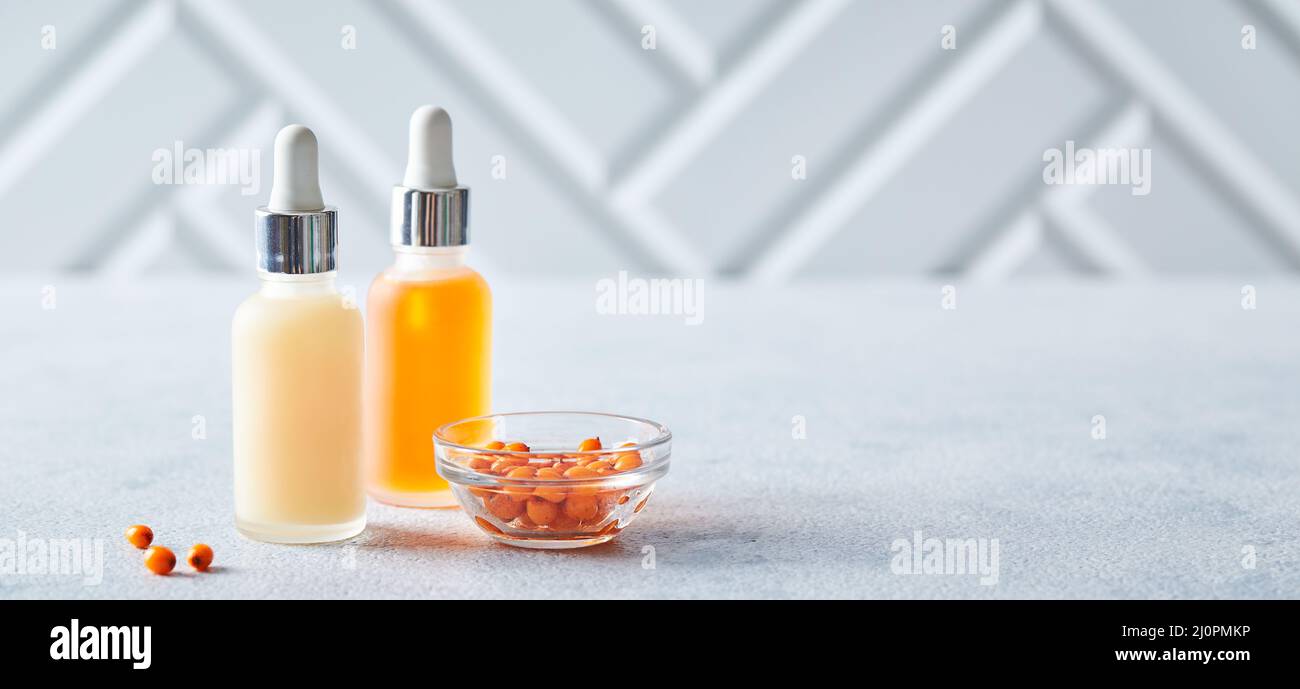 Bottiglie di vetro con prodotti per la cura della pelle del viso o del corpo con il seabackthorn su sfondo chiaro. Cura di sé, cosmetici, pratiche di bellezza, sel Foto Stock