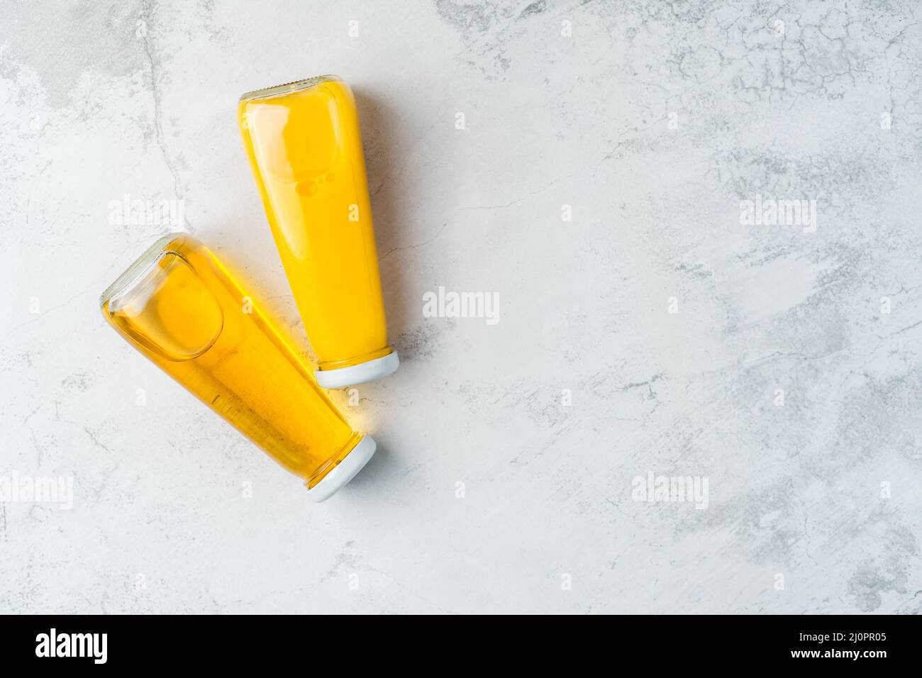 Bottiglie con succo liquido giallo halthy bevanda su sfondo grigio calcestruzzo. Succo d'arancia e di mela Foto Stock