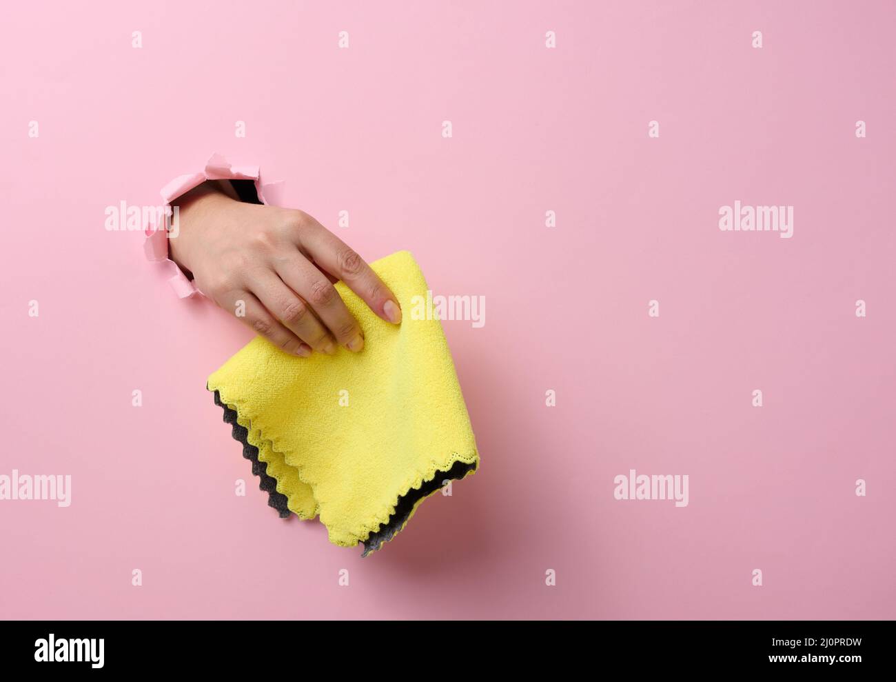 Mano femmina che sporge da un foro strappato in uno sfondo di carta rosa e che tiene uno straccio asciutto Foto Stock