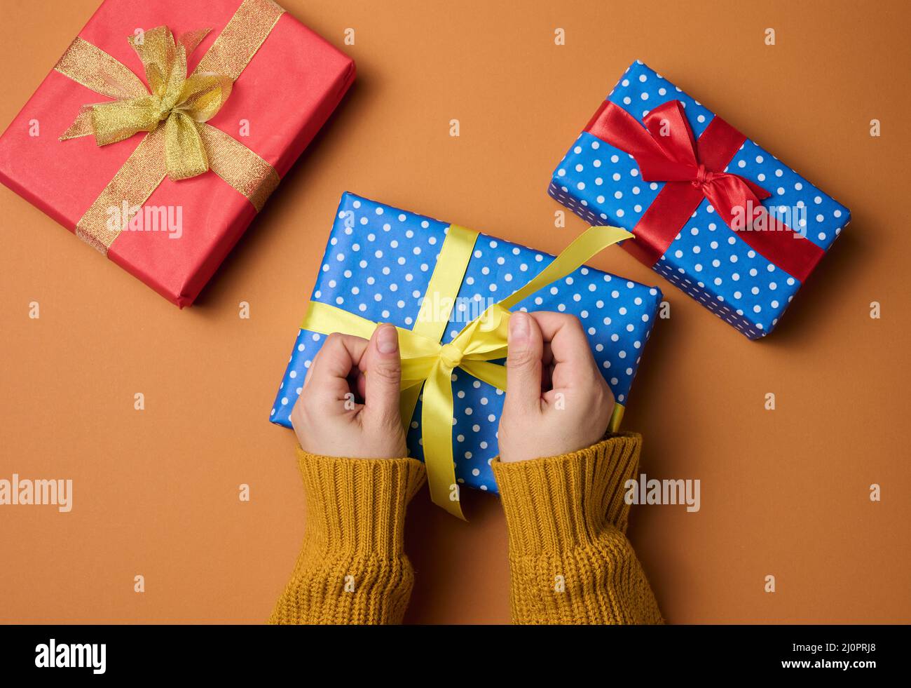 La mano femminile tiene una scatola avvolta con carta regalo su uno sfondo arancione. Preparazione di Natale Foto Stock