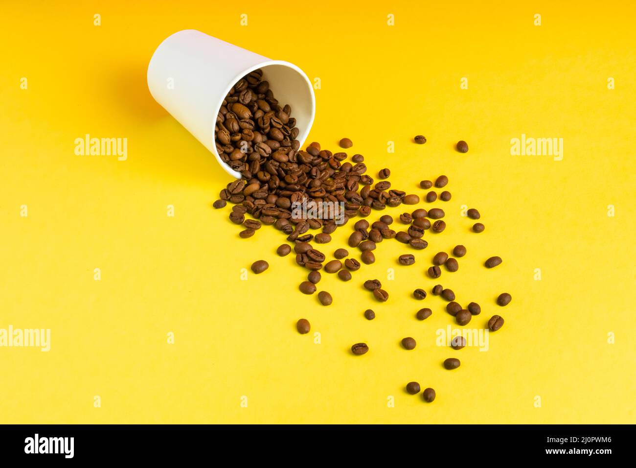 Tazza da caffè di carta bianca da asporto su sfondo giallo con i chicchi tostati che si versano fuori Foto Stock