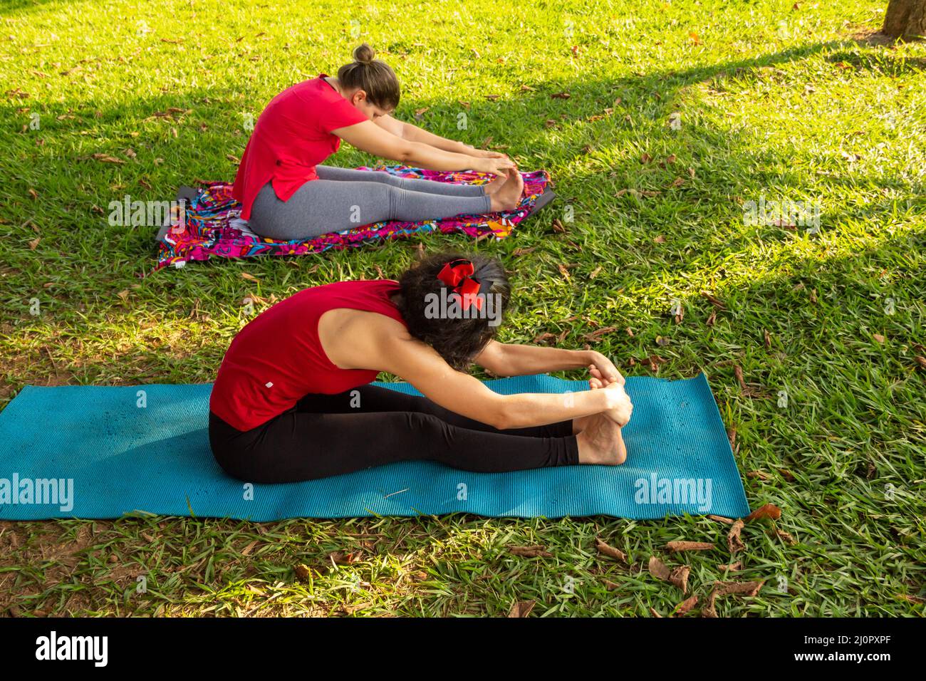 Goiânia, Goias, Brasile – 11 marzo 2022: Lezioni di yoga in un parco pubblico della città. Due persone che praticano lo yoga in un parco alberato e erboso. Foto Stock