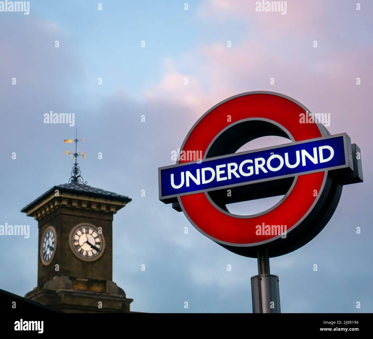 Guardando il cartello della metropolitana di London Transport e il simbolo accanto alla torre dell'orologio vittoriana della stazione di St Pancras nel cielo del tramonto, Londra, Inghilterra, Regno Unito Foto Stock