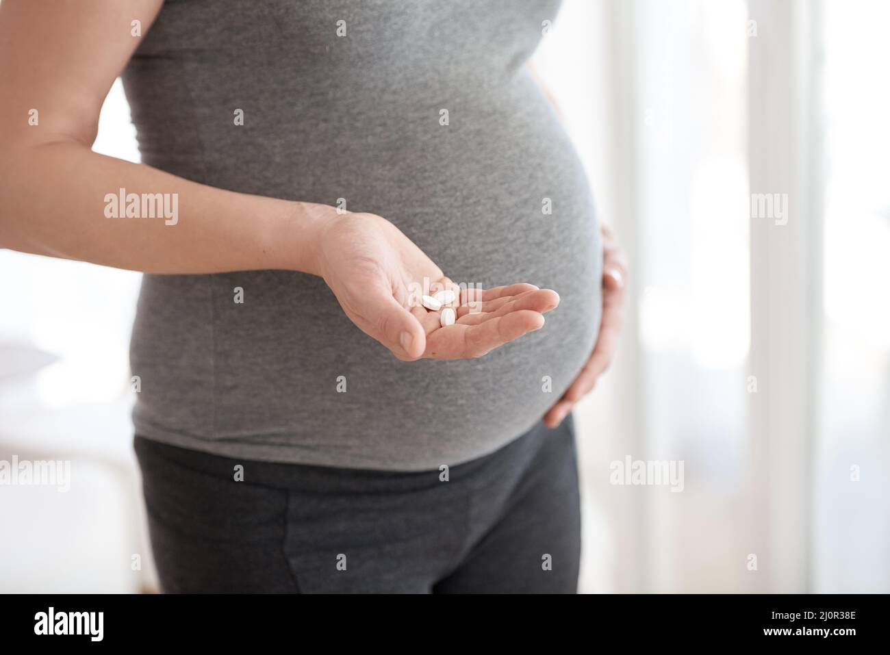 Le vitamine prenatali sono importanti per sviluppo adeguato. Scatto corto di una donna incinta che tiene le compresse mentre sta in piedi nella sua casa. Foto Stock