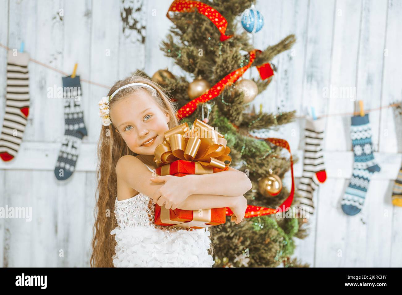 La ragazza sorridente tiene nelle sue mani una scatola regalo di Natale della Piazza Rossa con un nastro e un fiocco dorato lussureggiante. Natale e Capodanno Holi Foto Stock