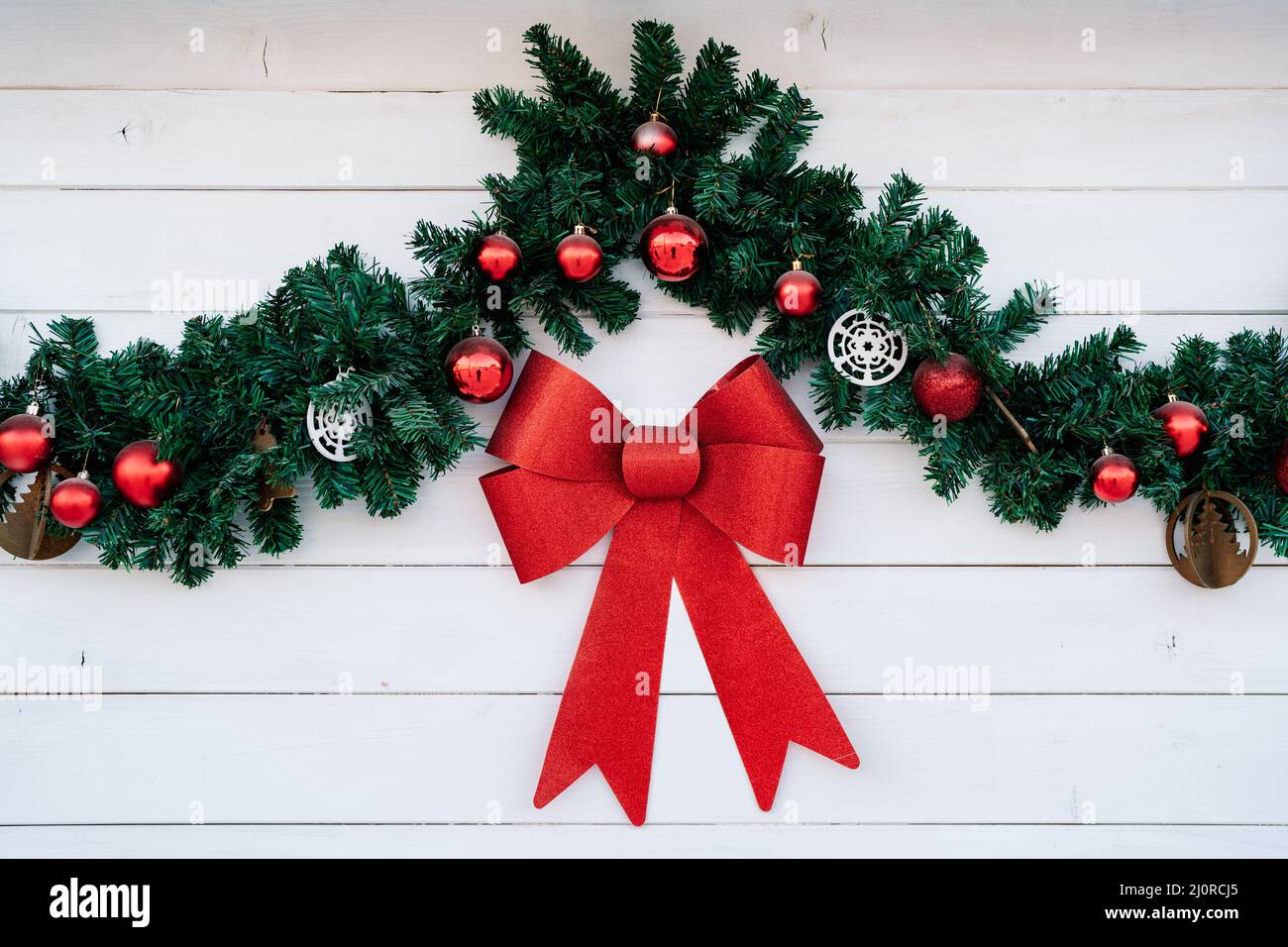 Decorazioni natalizie su sfondo bianco di legno - un ramo di abete con palline rosse e un grande arco rosso. Foto Stock