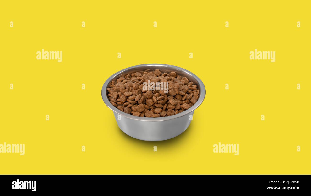 Gli alimenti per animali domestici sono asciutti in una ciotola isolata su sfondo giallo dello studio Foto Stock