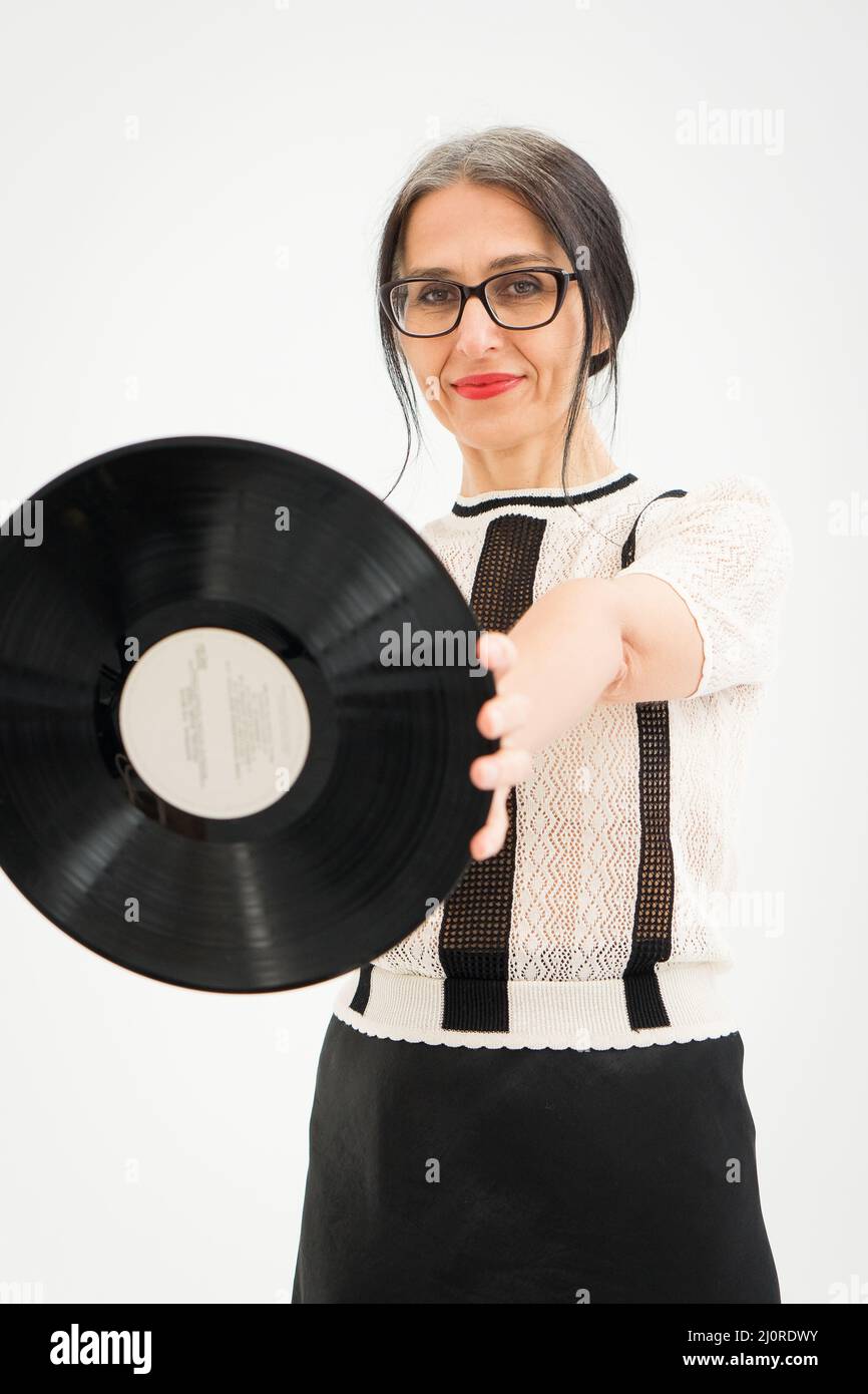 Studio foto di donna di mezza età che inizia a ottenere grigio-capelli indossando abiti bianchi e neri con vinile record in mani su sfondo bianco, al centro Foto Stock