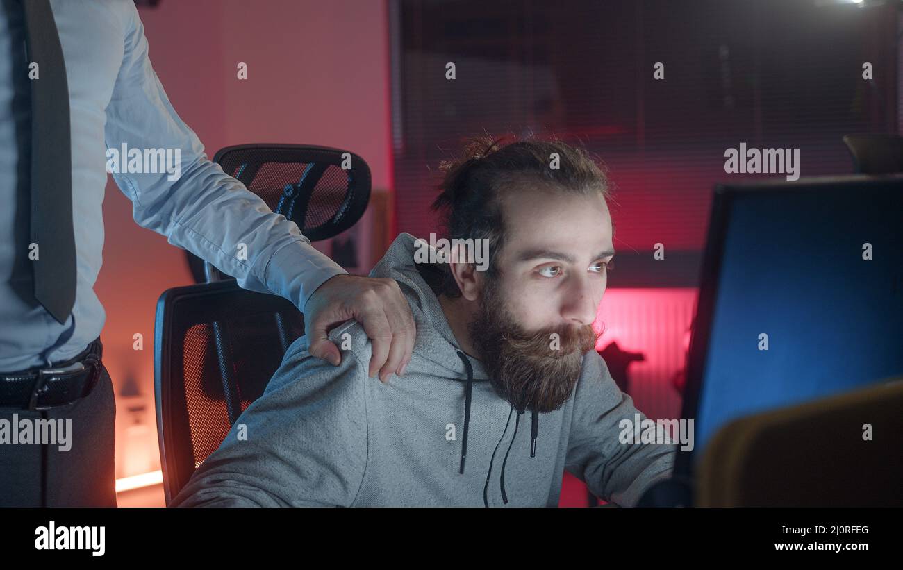 Bearded haired lungo-haired hippie guardando l'uomo che gioca ai giochi al calcolatore, l'uomo del datore di lavoro mette la sua mano su hippie guardando la spalla dell'adolescente che chiede che cosa Foto Stock