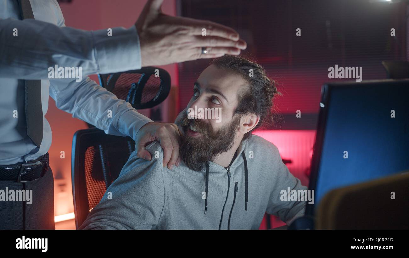 Hippie lungo-capelli osservare uomo che gioca ai giochi al calcolatore, uomo del datore di lavoro mette la sua mano su hippie osservare la spalla del adolescente che chiede che cosa sta facendo Foto Stock