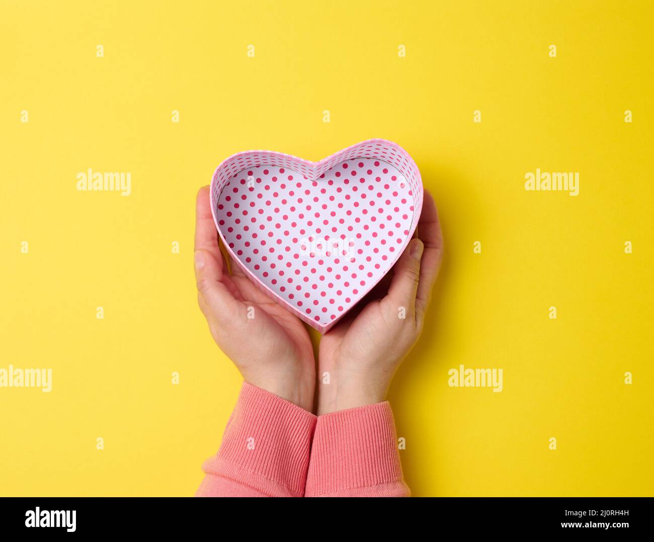 Le mani femminili tengono aperta la scatola del regalo di cartone quadrata su uno sfondo giallo, vista dall'alto Foto Stock