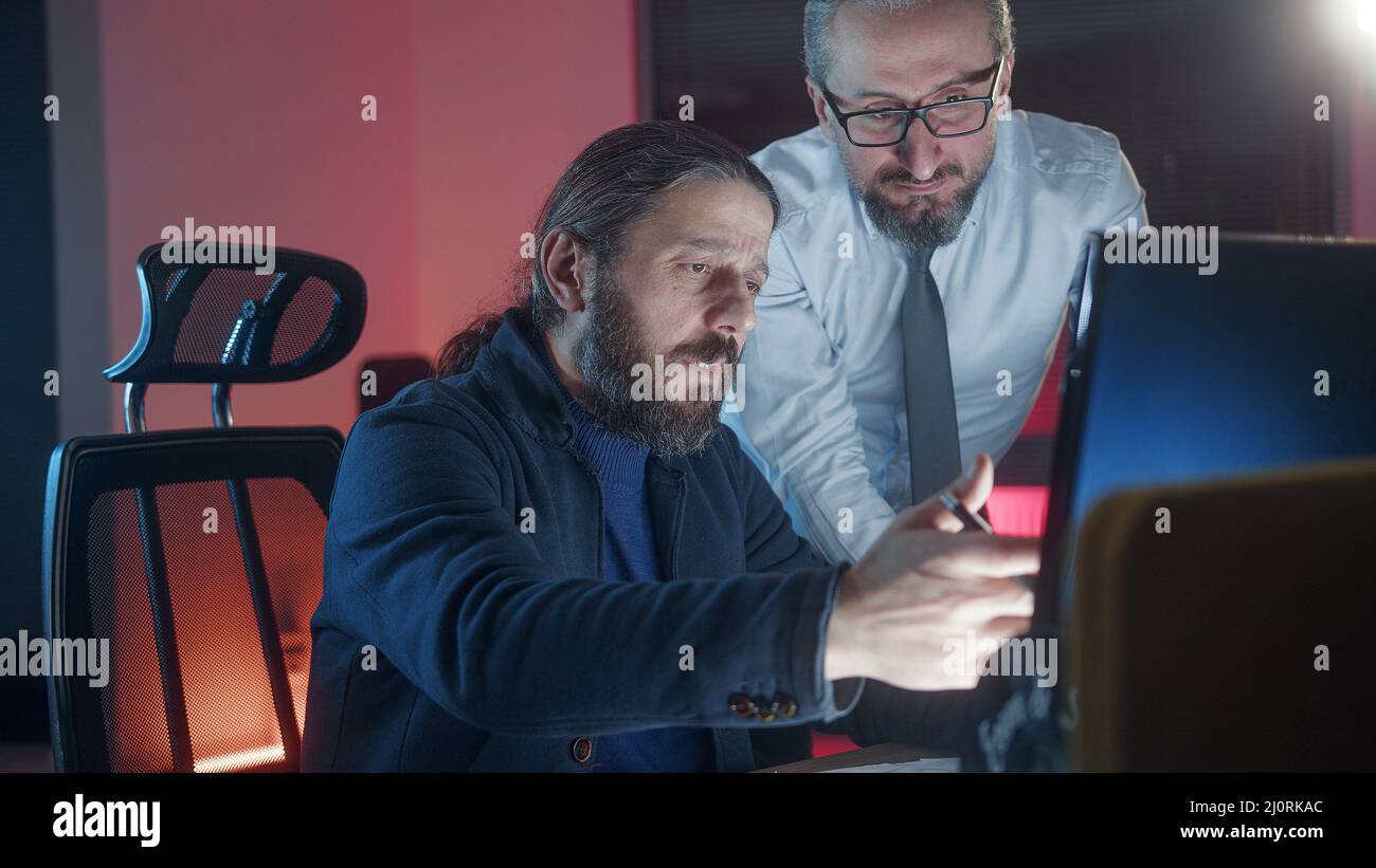 Due colleghi maschi che collaborano in ufficio mentre guardano insieme lo schermo del computer sul posto di lavoro. Concetto di ufficio Foto Stock