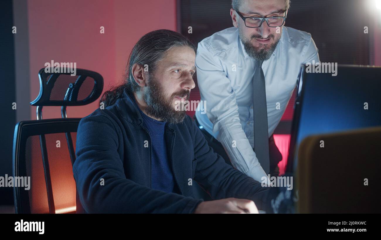 Due colleghi maschi che collaborano in ufficio mentre guardano insieme lo schermo del computer sul posto di lavoro. Foto Stock