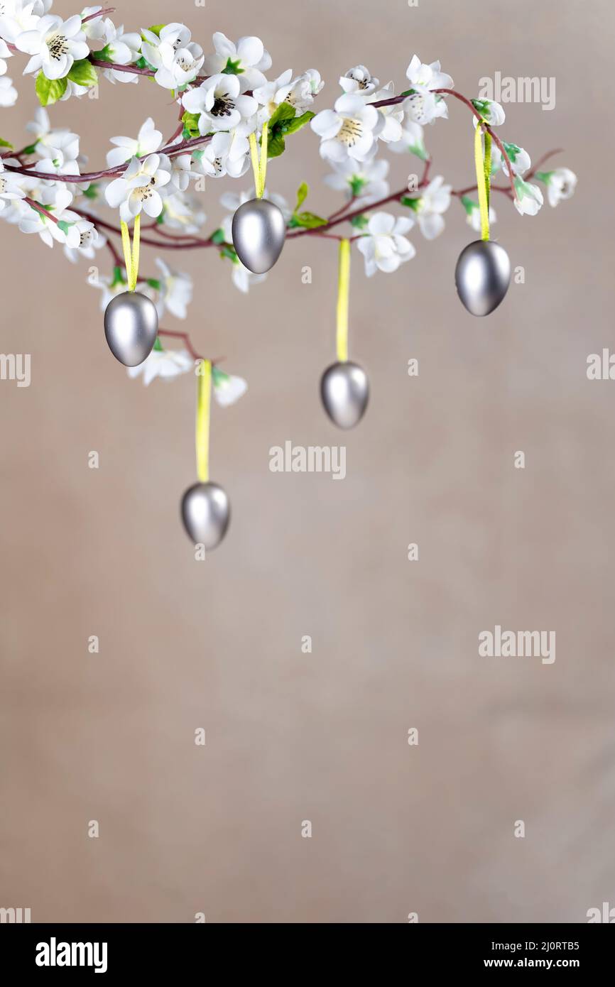 Uova di Pasqua color argento appese sul ramo con fiori bianchi Foto Stock
