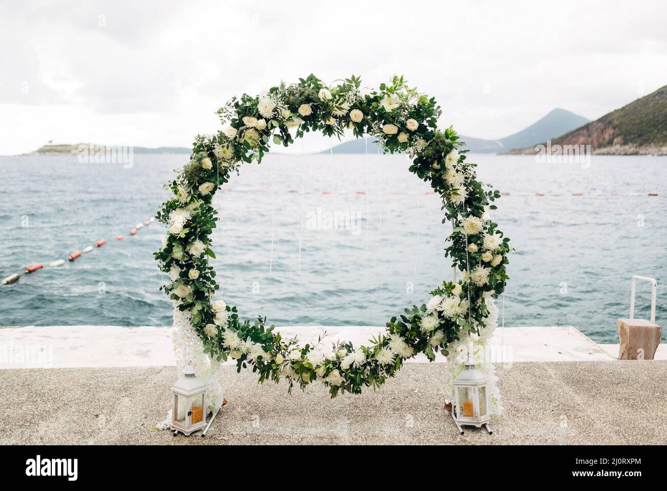 Arco di nozze rotondo tessuto di rose e foglie verdi si erge sul molo Foto Stock