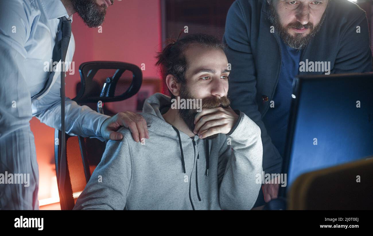 Tre colleghi maschi che collaborano in ufficio mentre guardano insieme lo schermo del computer sul posto di lavoro. Concetto di ufficio Foto Stock