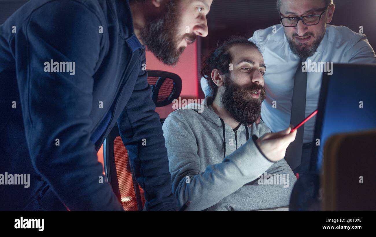 Tre colleghi maschi che collaborano in ufficio mentre guardano insieme lo schermo del computer sul posto di lavoro Foto Stock