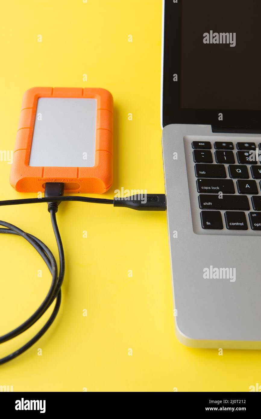 Disco rigido esterno su sfondo giallo collegato alla porta USB di un computer portatile Foto Stock