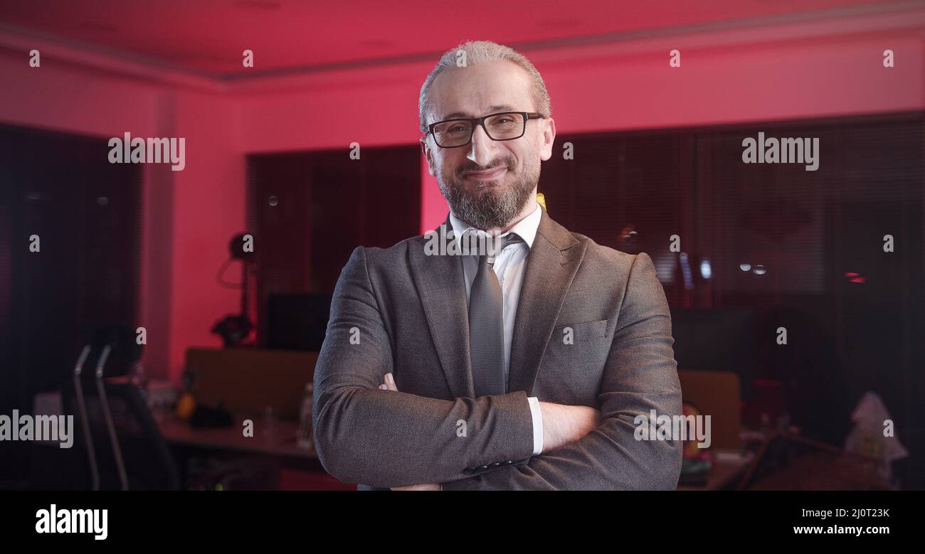 Ritratto di top manager bearded di mezza età in tuta da ufficio e occhiali. Uomo d'affari felice di successo in piedi, sorridente e guardando la macchina fotografica Foto Stock