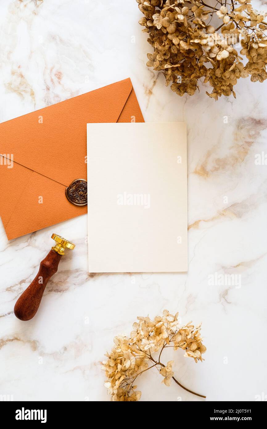 Design di carte di invito per matrimoni di lusso. Carta bianca, busta di bronzo, fiori secchi su tavolo da scrivania in marmo vista dall'alto. Foto Stock