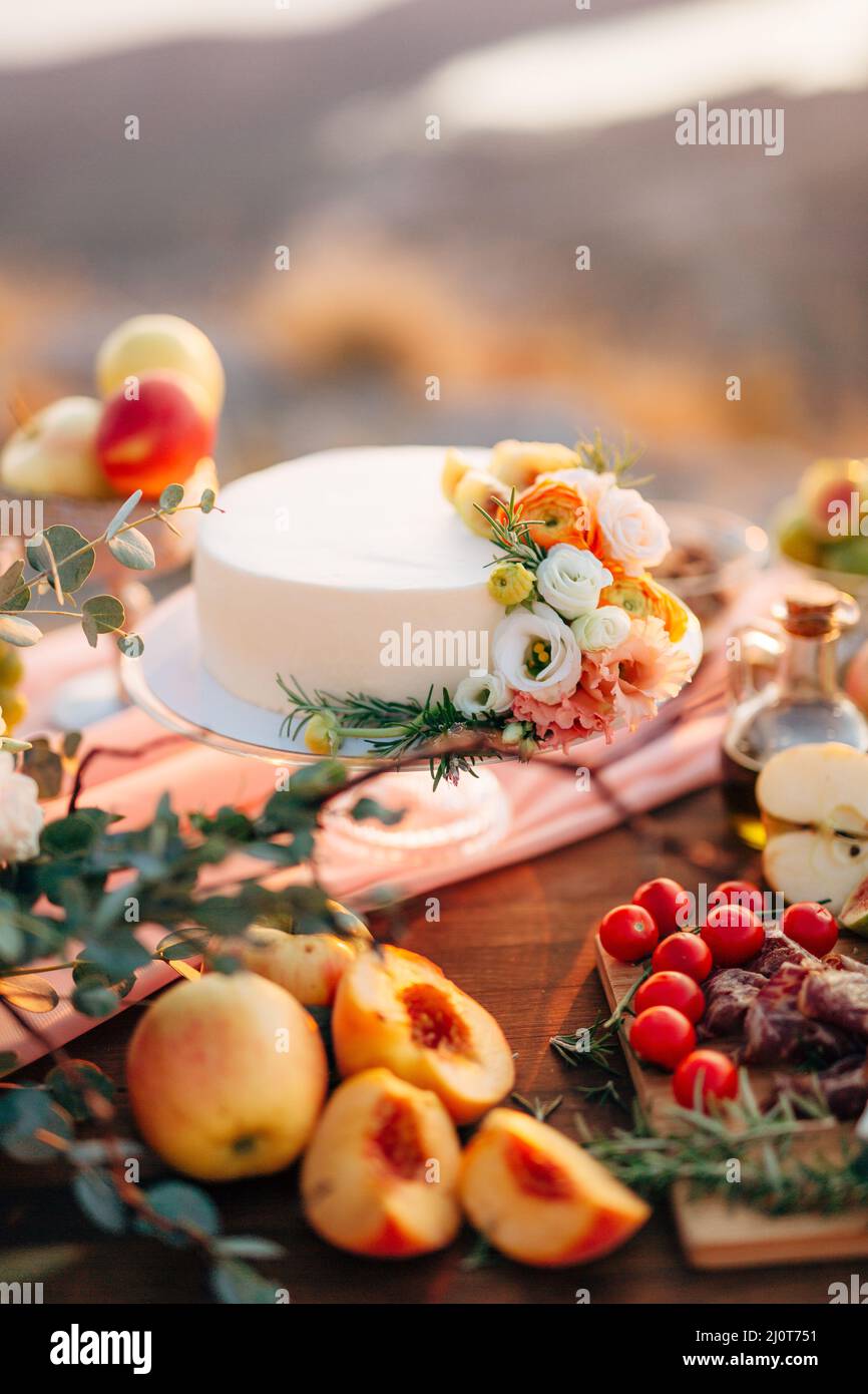 Torta nuziale decorata con fiori si erge su un tavolo tra frutta e verdura Foto Stock