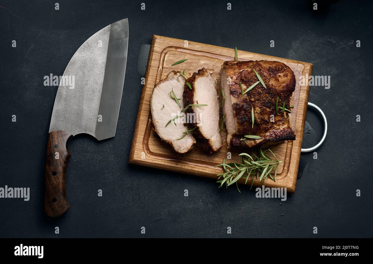 Pezzo di carne di maiale al forno in spezie su un asse di legno, tagliato a pezzi Foto Stock