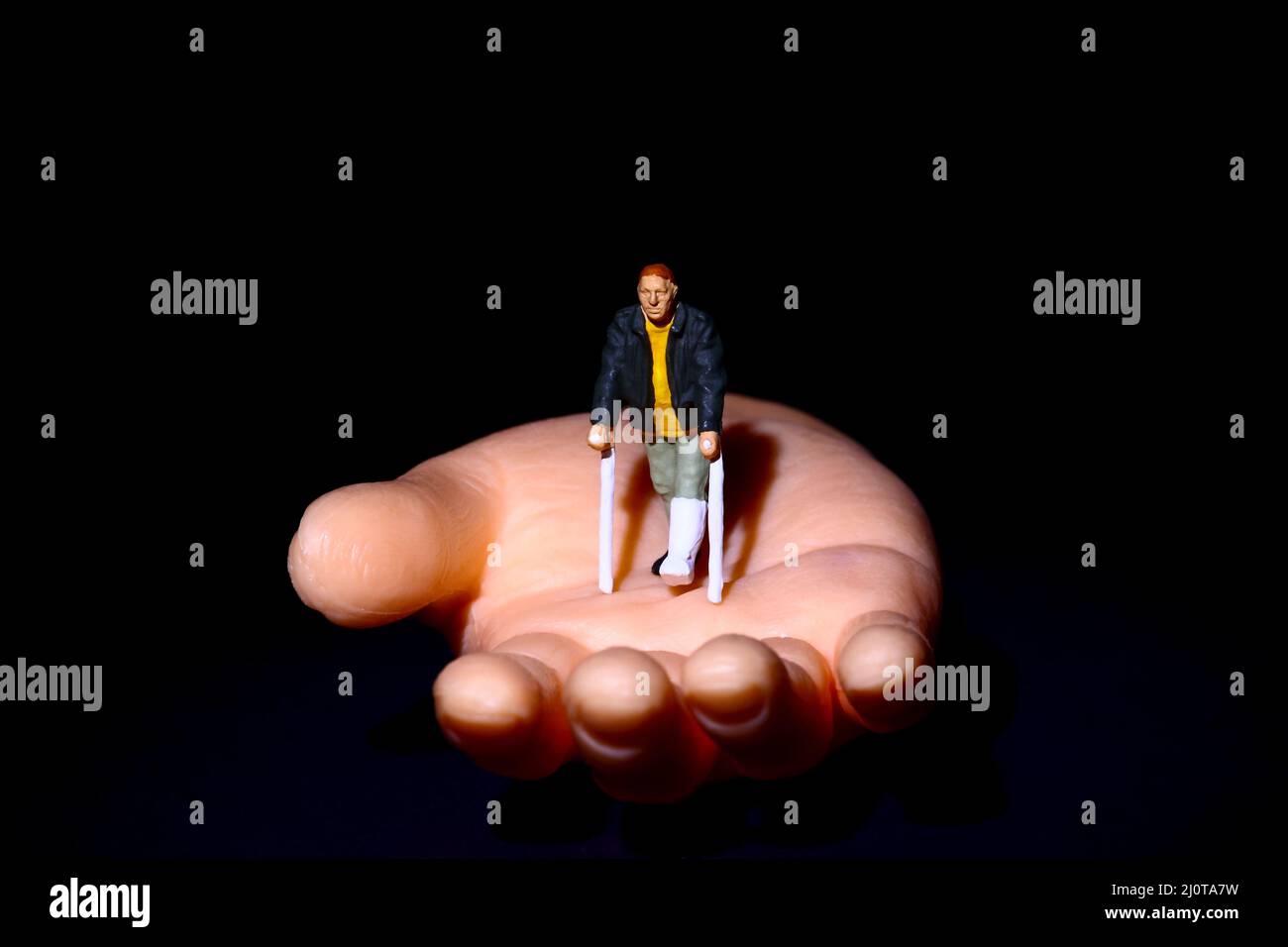 Personaggio uomo in miniatura con stampelle sedette su una mano falsa disabile aiutante concetto di mano Foto Stock