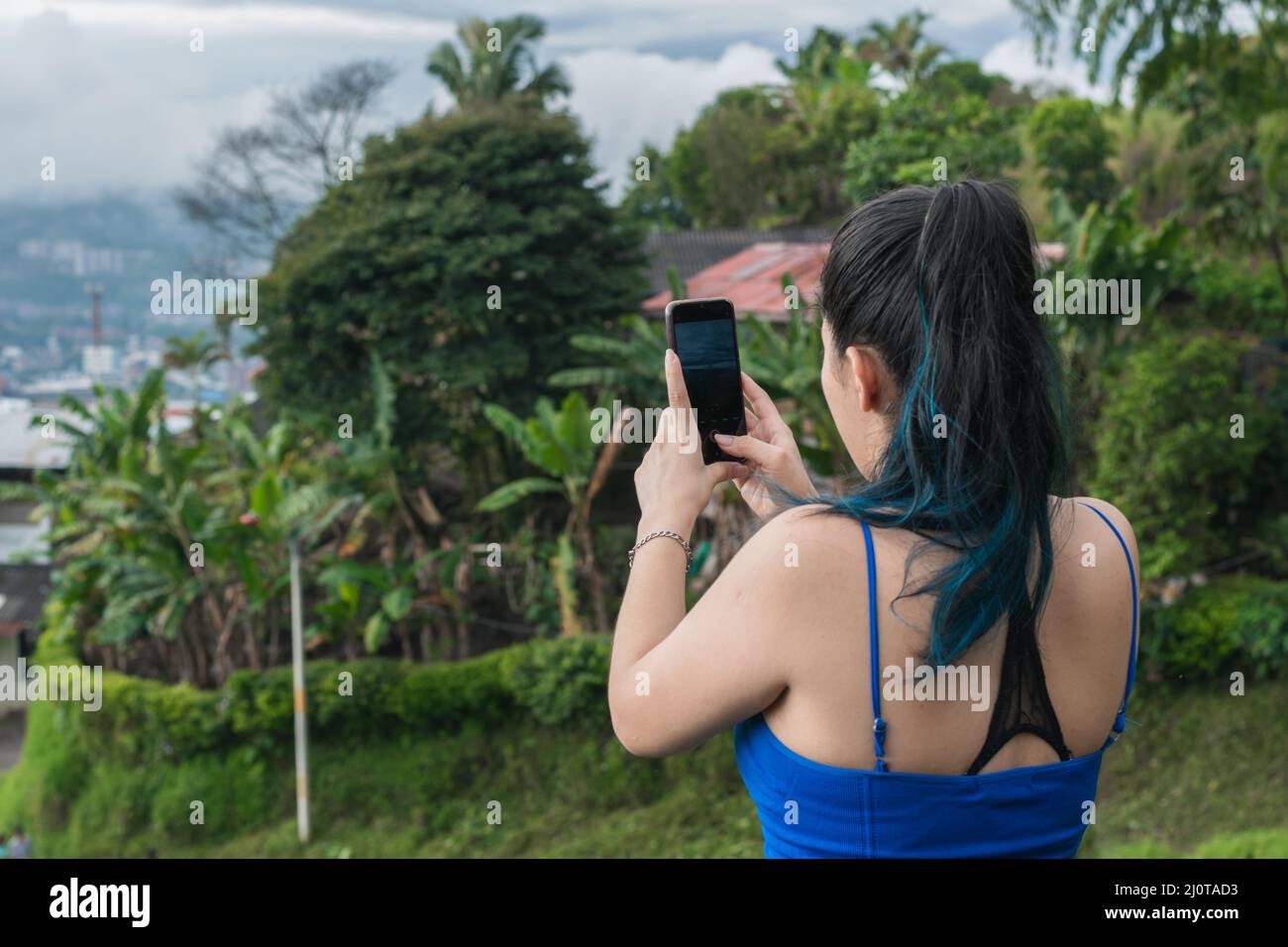 giovane donna latina con capelli blu che scattano una foto di un paesaggio nelle belle montagne colombiane. influencer ragazza che crea contenuto per la sua socia Foto Stock