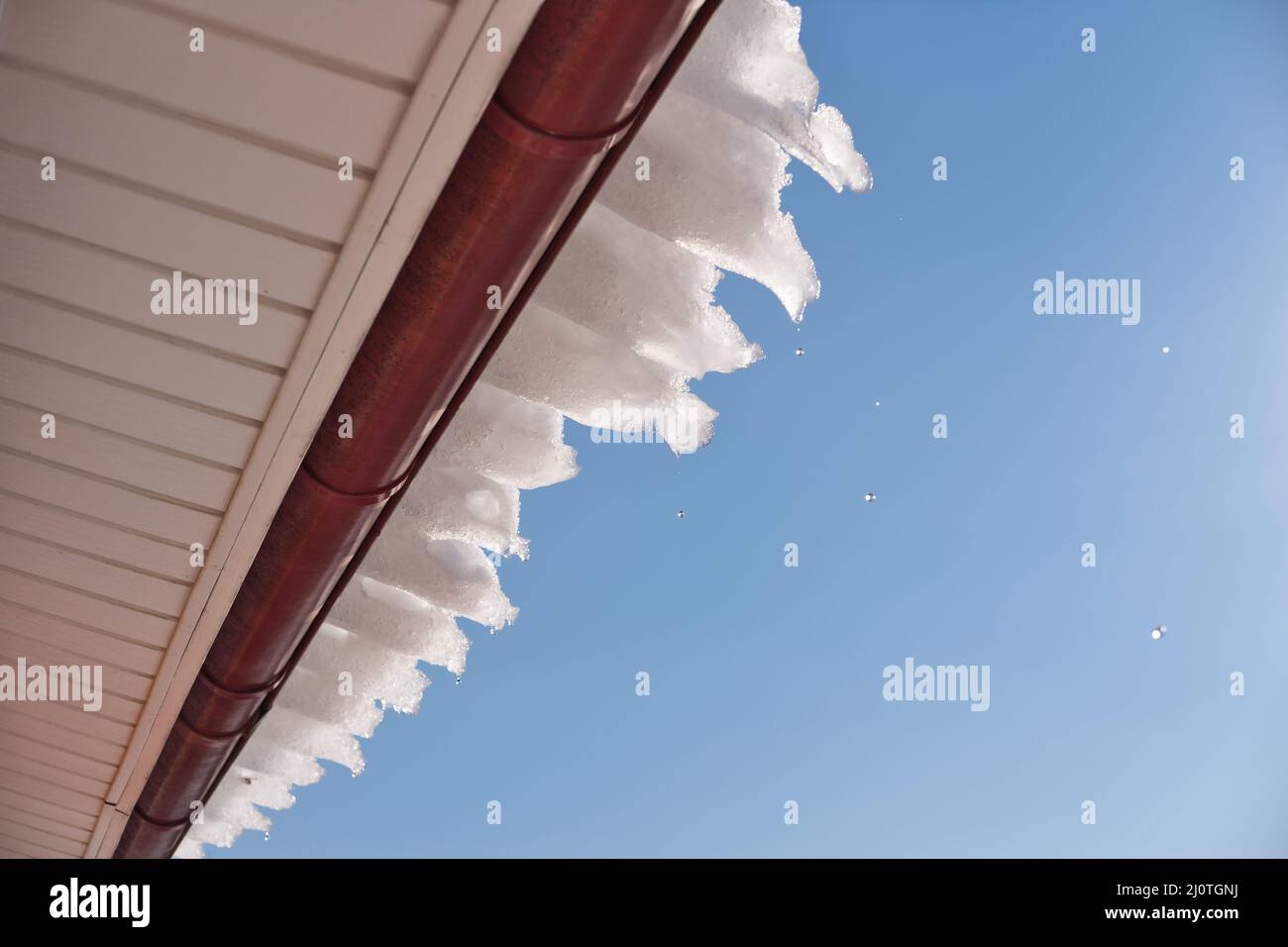 Gocce d'acqua che cadono dal tetto contro il cielo azzurro. Neve che si scioglie all'inizio della stagione primaverile. Foto Stock