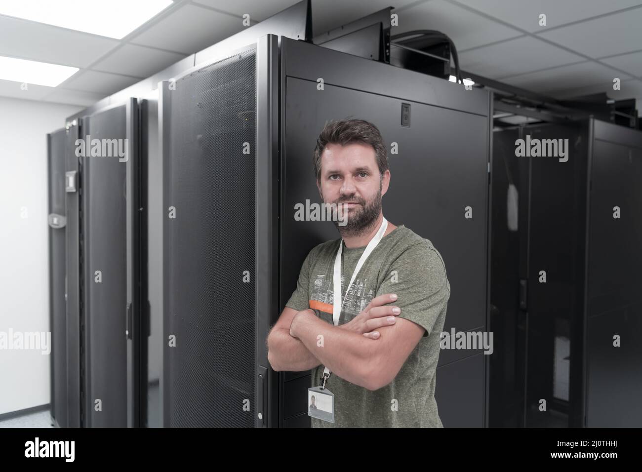 Ritratto di un tecnico maschile o di un amministratore di rete coraggioso come un eroe con le braccia incrociate nella sala server del data center. Foto Stock