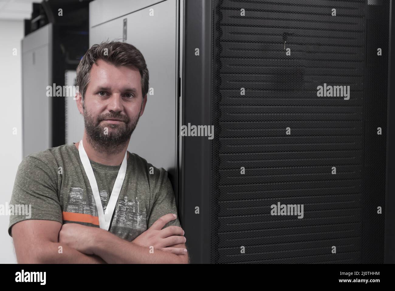 Ritratto di un tecnico maschile o di un amministratore di rete coraggioso come un eroe con le braccia incrociate nella sala server del data center. Foto Stock