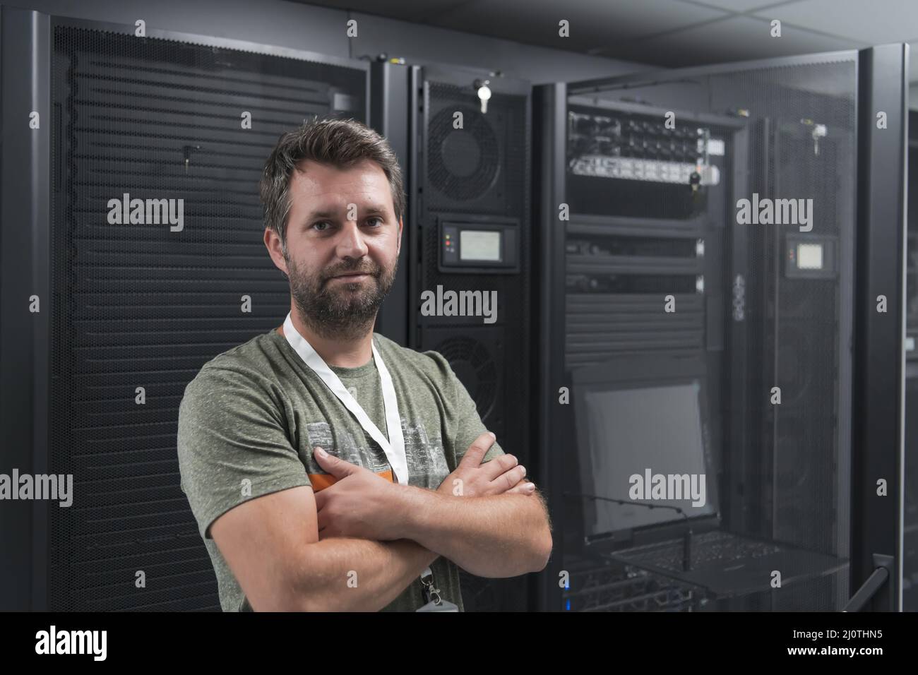 Ritratto di un tecnico maschile o di un amministratore di rete coraggioso come un eroe con le braccia incrociate nella sala server del data center. Foto Stock