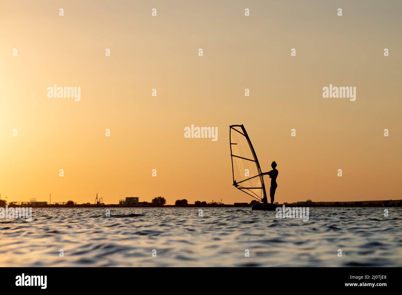 Silhouette di una giovane donna kitesurfer al tramonto. Allenamenti in clima calmo sull'estuario Foto Stock