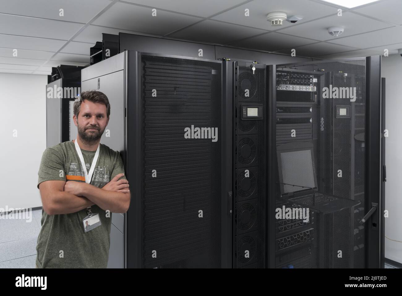 Ritratto di un tecnico maschile o di un amministratore di rete coraggioso come un eroe con le braccia incrociate nella sala server del data center. Foto Stock
