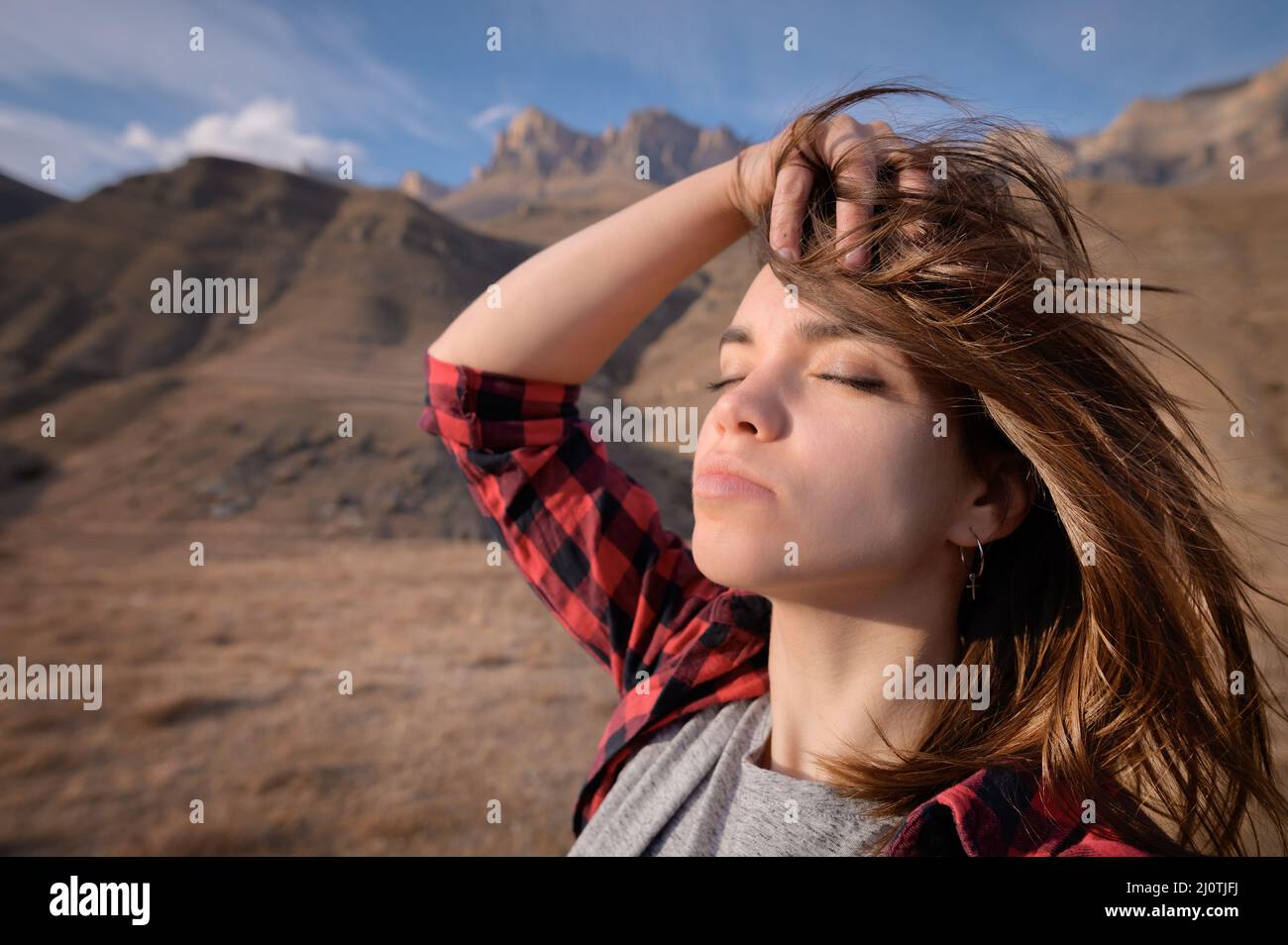 Ritratto di attraente giovane caucasica che gode di occhi chiusi si erge in montagna sullo sfondo di rocce epiche Foto Stock