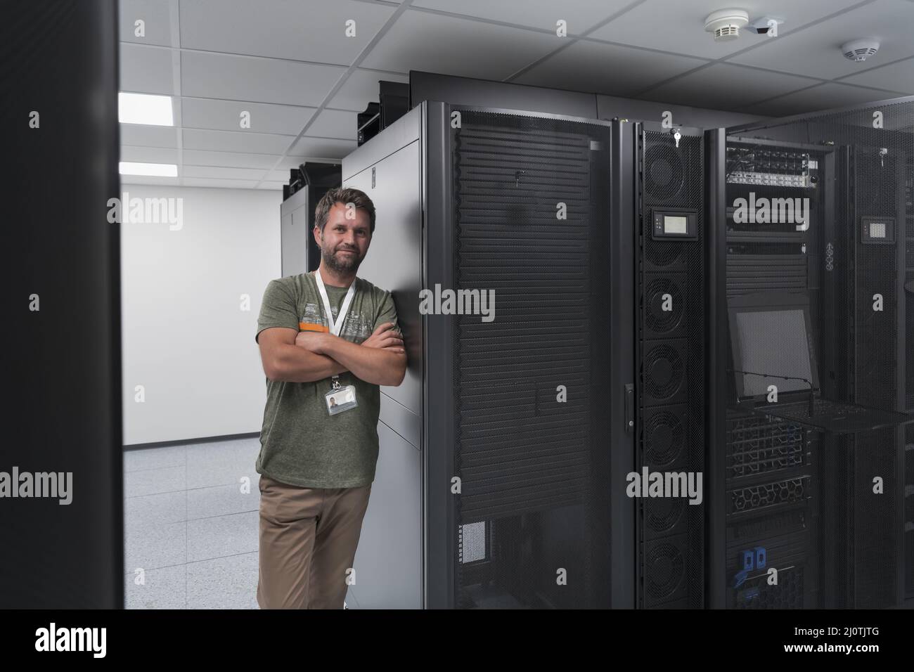 Ritratto di un tecnico maschile o di un amministratore di rete coraggioso come un eroe con le braccia incrociate nella sala server del data center. Foto Stock