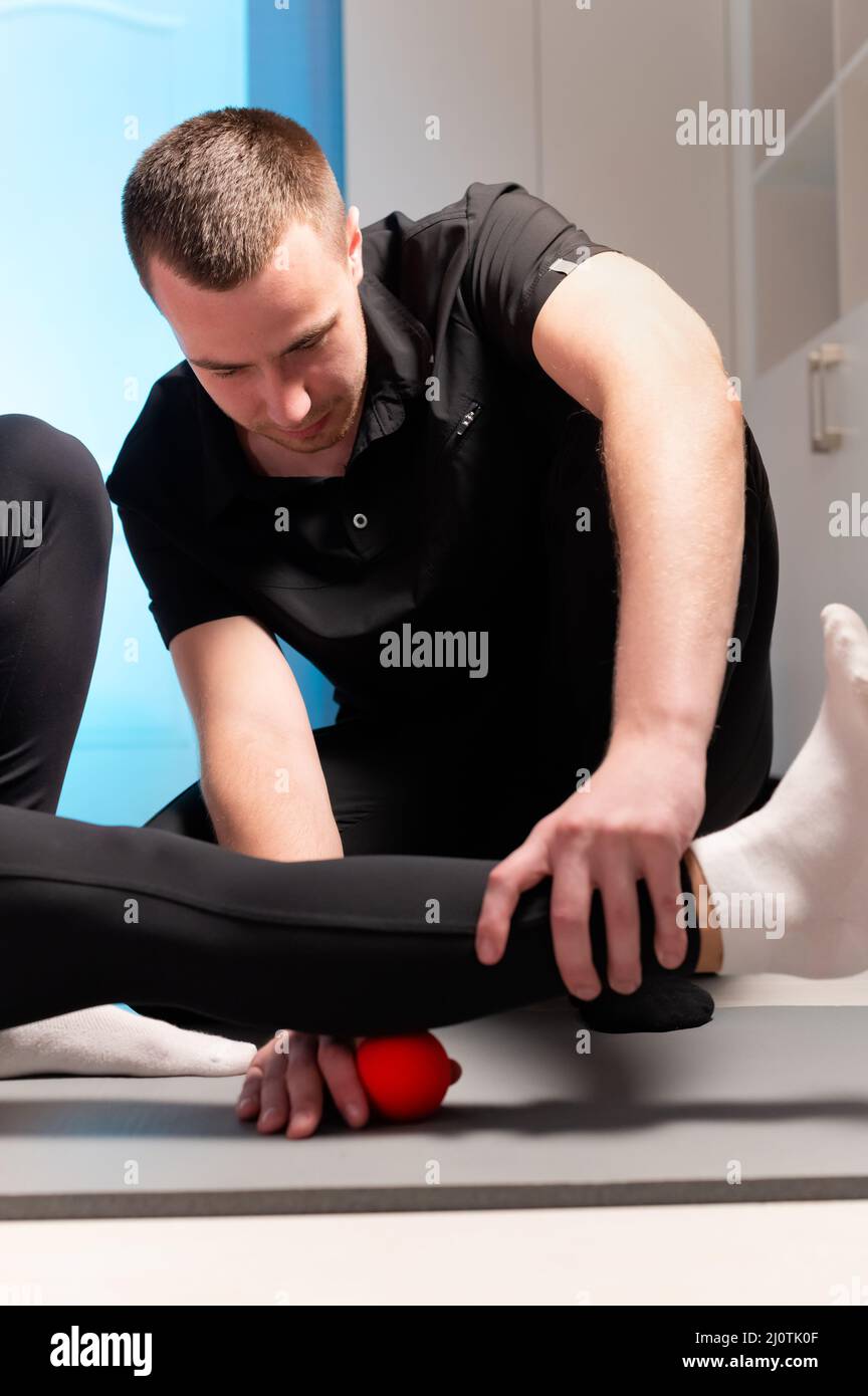 Un giovane massaggiatore maschile insegna ad un cliente caucasico donna miofasciale auto-massaggio utilizzando una palla da massaggio al chiuso. Miofasceo Foto Stock