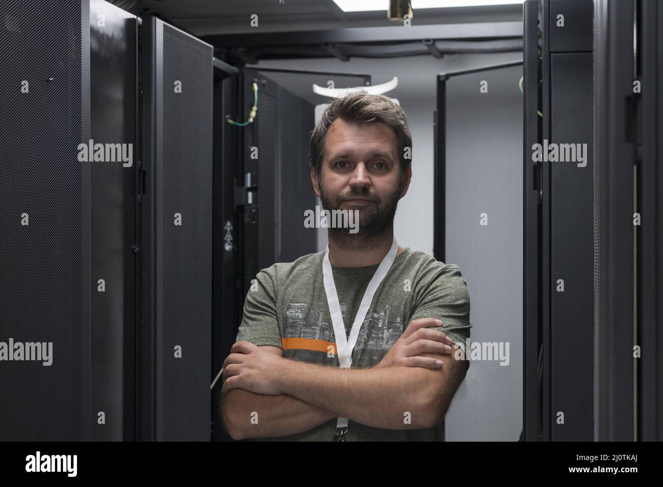 Ritratto di un tecnico maschile o di un amministratore di rete coraggioso come un eroe con le braccia incrociate nella sala server del data center. Foto Stock