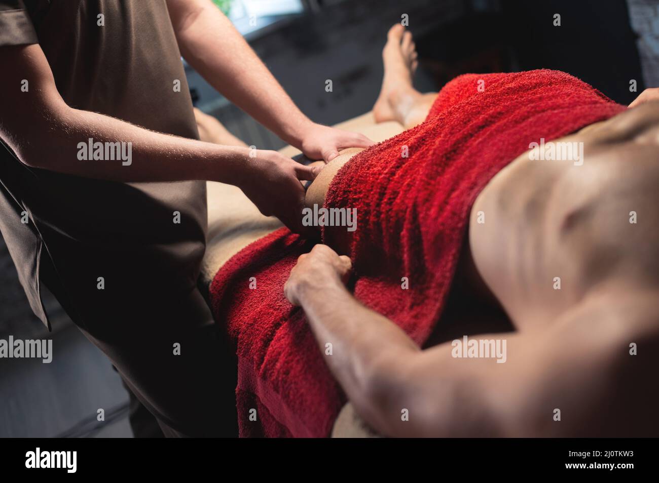 Massaggio sportivo professionale maschile dell'anca e del ginocchio in una sala massaggi scura. Spazio di copia Foto Stock