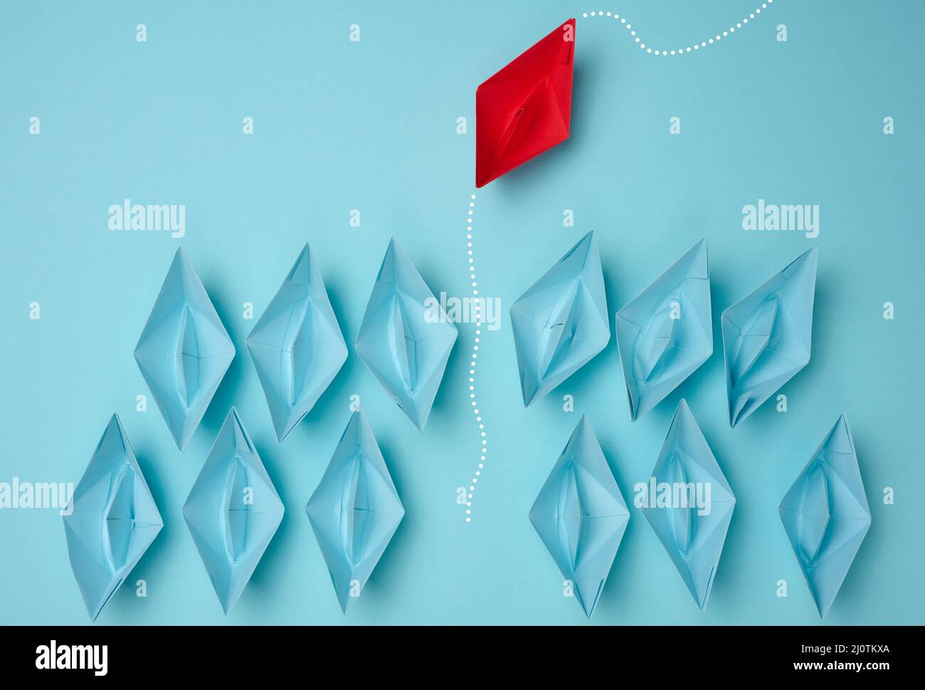 Un gruppo di barche di carta blu che si dirigono in una direzione e una rossa che si dirigono nella direzione opposta. Il concetto di individua Foto Stock