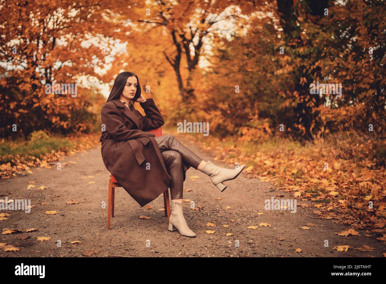 Ritratto di una giovane donna con vecchia poltrona in un cappotto marrone in autunno Foto Stock