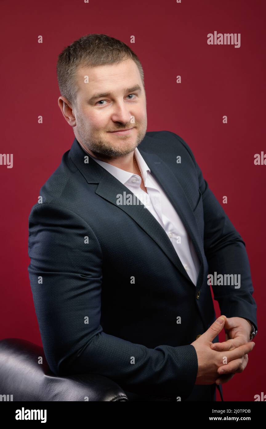 Fidato leader di affari o manager in piedi appoggiandosi alla sua sedia in studio, braccia incrociate, sorridendo alla fotocamera. Cauc Foto Stock