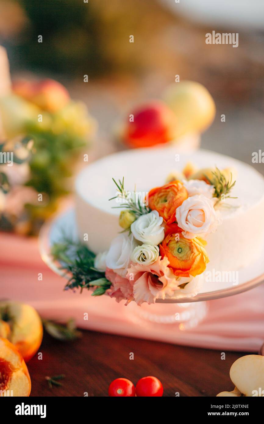 Torta nuziale bianca decorata con rose si erge su un tavolo Foto Stock