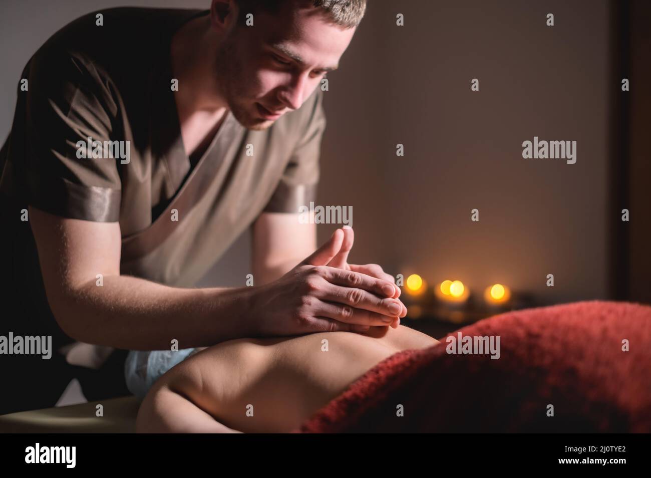 Massaggio professionale della schiena e della parte inferiore della schiena. Massaggiatore maschile massaggia un cliente a una donna in una stanza buia a lume di candela Foto Stock
