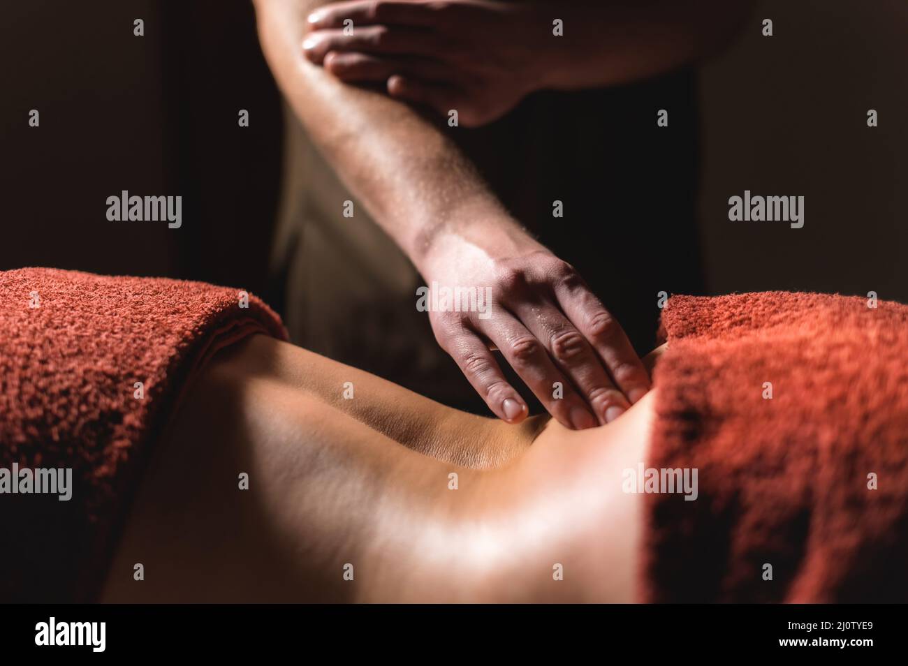 Massaggio professionale della schiena e della parte inferiore della schiena. Massaggiatore maschile massaggia un cliente a una donna in una stanza buia a lume di candela Foto Stock