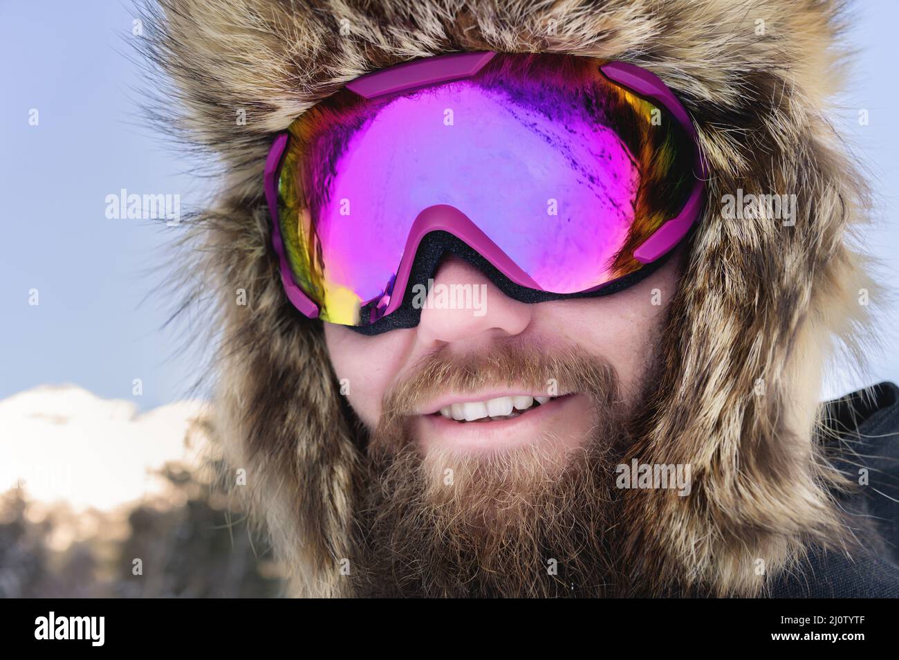 Primo piano ritratto di un felice sciatore bearded snowboarder in una maschera da sci con occhiali e un grande cappello di pelliccia vecchia scuola su sfondo o Foto Stock