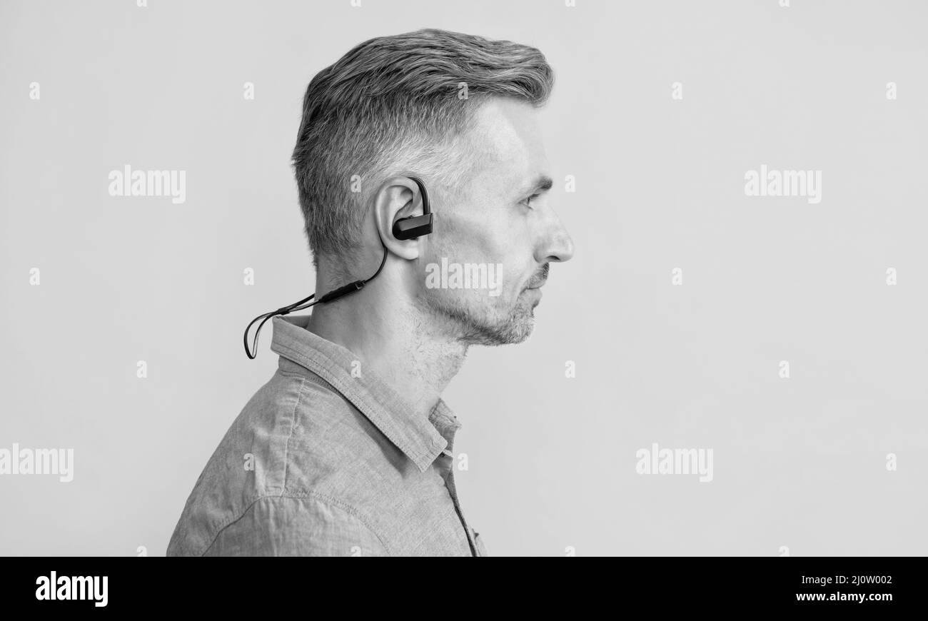 profilo di uomo maturo in moderni auricolari wireless su sfondo giallo, tecnologia Foto Stock