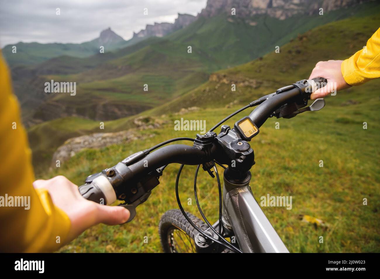 Un primo piano del ciclista a mano della ragazza sul manubrio di una mountain bike sullo sfondo di rocce e montagne epiche. MOU Foto Stock