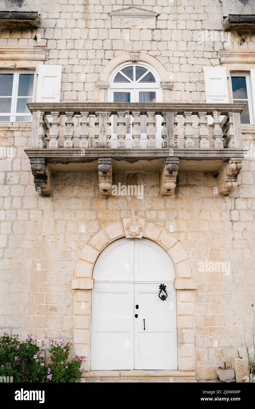 Balcone in pietra su una facciata in mattoni di un vecchio edificio con una porta bianca in legno ad arco Foto Stock