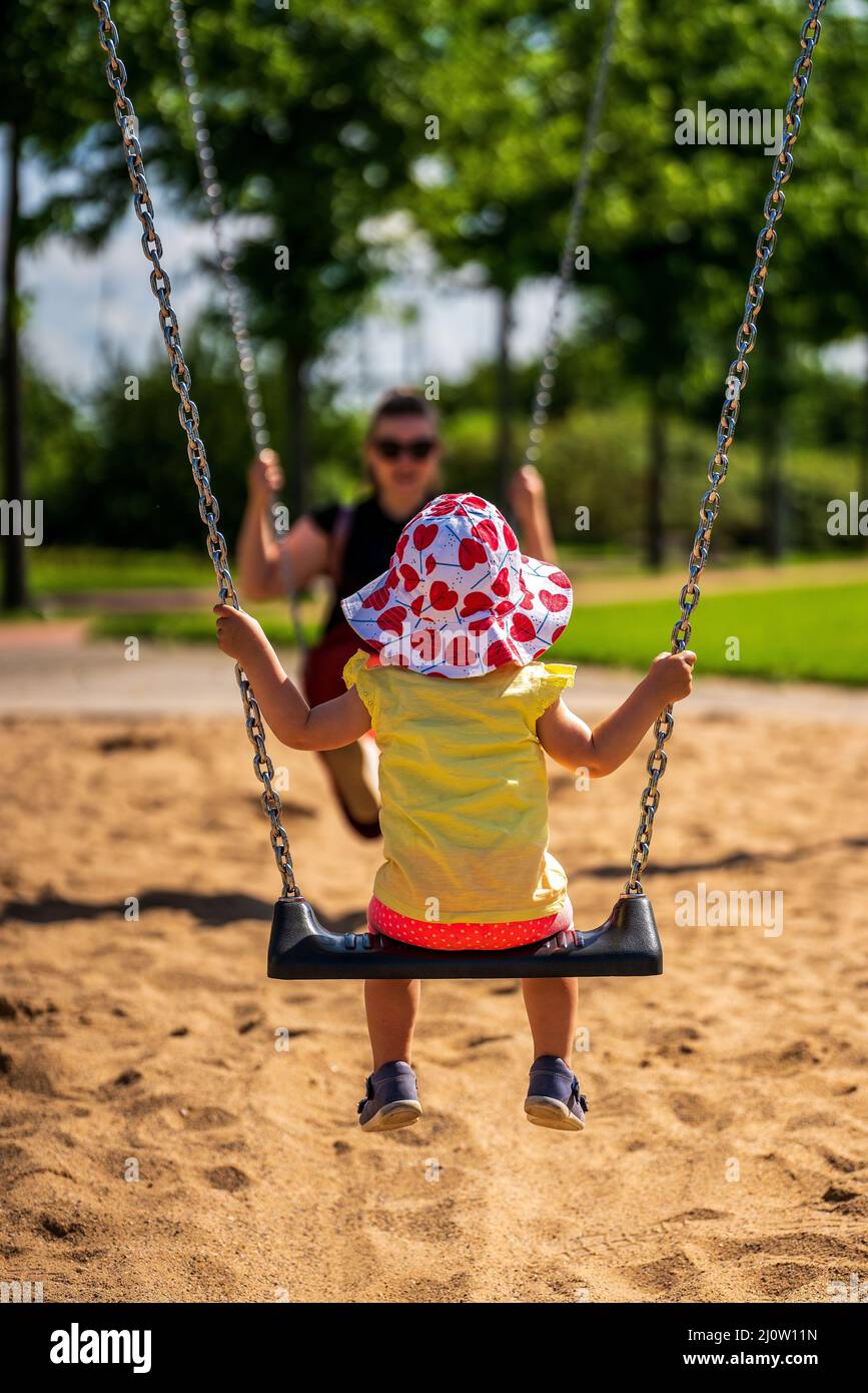 Un bambino giovane con una donna in altalena in un parco giochi Foto Stock